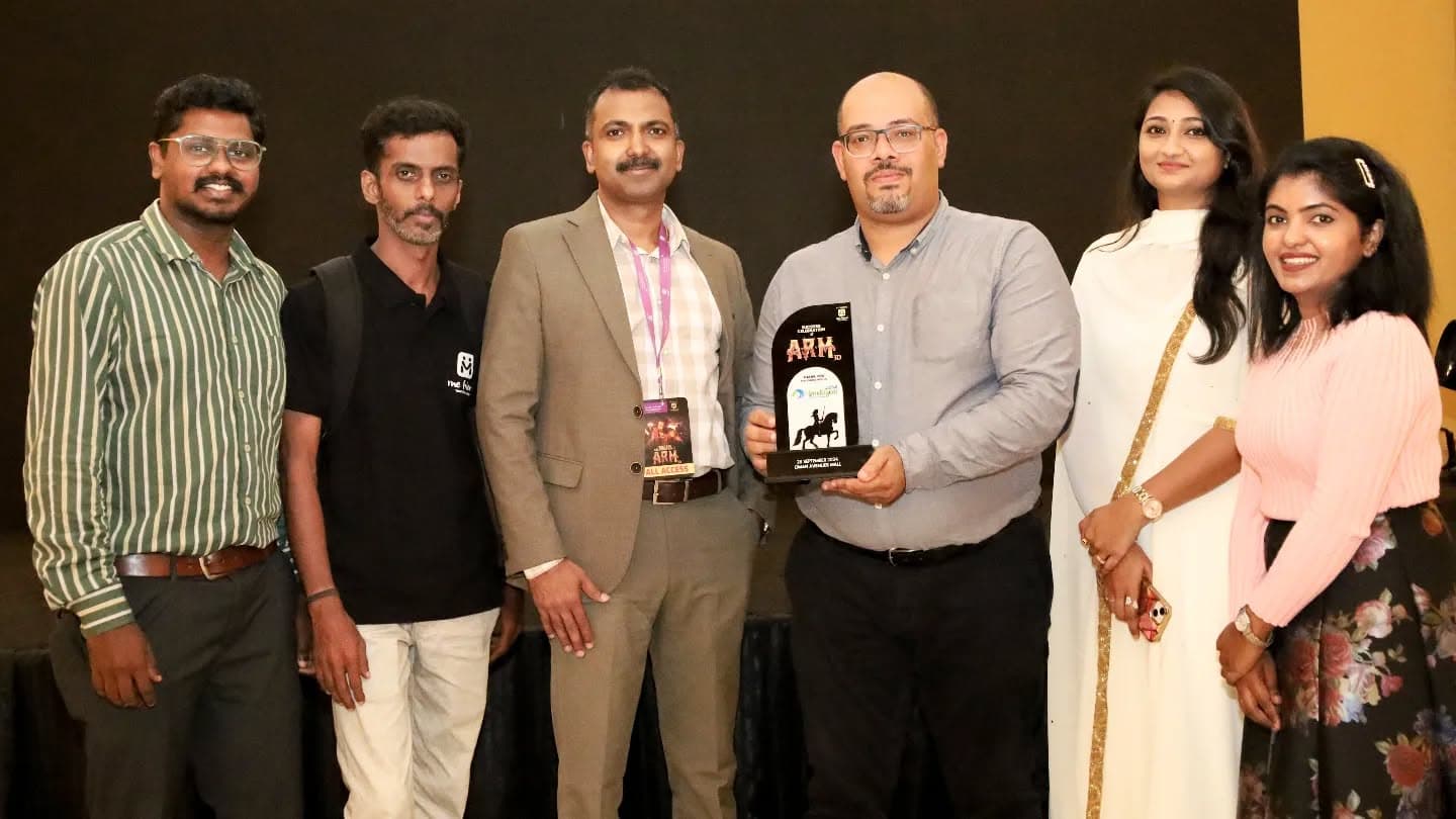 Six people posing at an event, one man holding a black ARM success award.