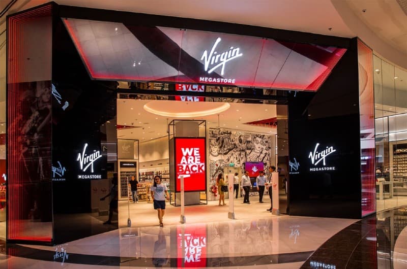 Modern Virgin Megastore entrance with a red "WE ARE BACK" sign and shoppers walking inside.